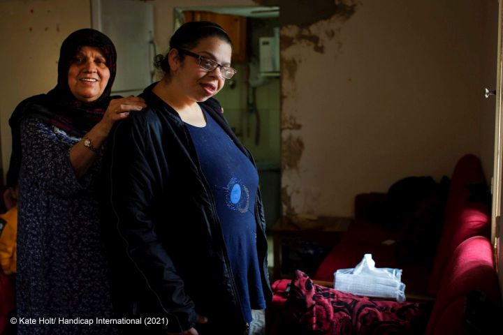 A Syrian woman living in Lebanon is standing in front of a camera together with her granddaughter who has an intellectual impairment.